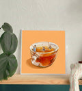 Framed artwork of a glass teacup with tea and small figures on an orange background.